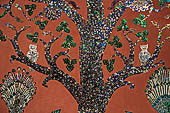 Wat Xieng Thong temple in Luang Prabang, Laos. Detail of the famous tree of life mosaic of the back wall of the sim, in colored glass on a dark red background. 